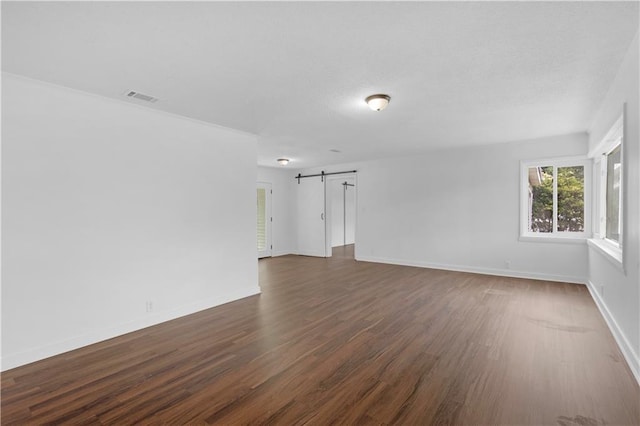 unfurnished room with dark wood-style floors, baseboards, visible vents, and a barn door