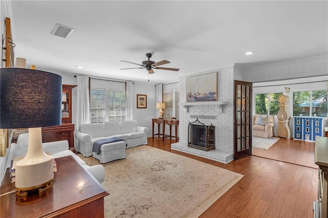 living room with ceiling fan, a brick fireplace, and hardwood / wood-style floors