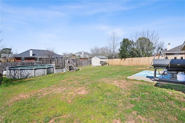 view of yard with a fenced in pool, a fenced backyard, an outbuilding, a wooden deck, and a shed