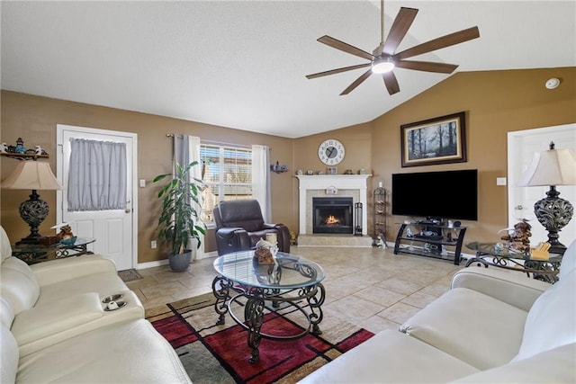 living room with vaulted ceiling, ceiling fan, a tiled fireplace, and baseboards