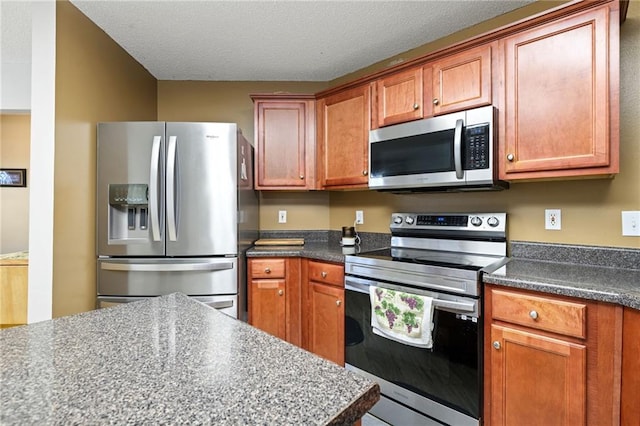 kitchen with stainless steel appliances, dark countertops, brown cabinets, and a textured ceiling