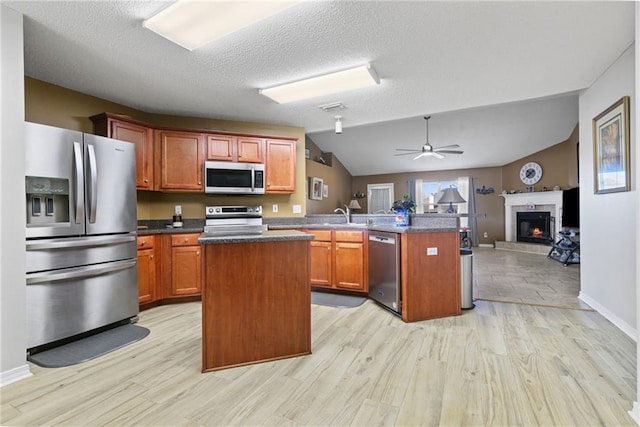 kitchen with a tile fireplace, stainless steel appliances, a peninsula, light wood-style floors, and open floor plan