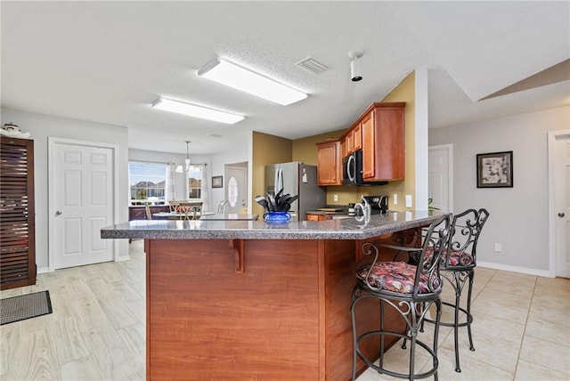 kitchen with a breakfast bar, visible vents, freestanding refrigerator, brown cabinetry, and dark countertops