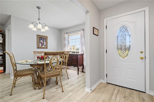 dining space featuring a chandelier, a textured ceiling, light wood-type flooring, and baseboards