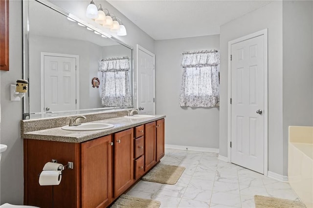 bathroom with marble finish floor, a bathing tub, baseboards, and a sink