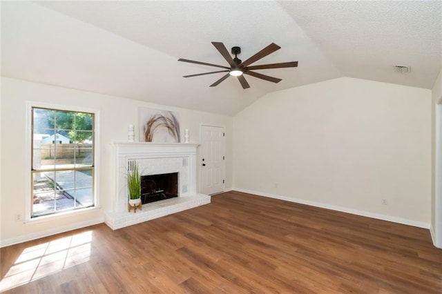 unfurnished living room featuring a ceiling fan, lofted ceiling, a brick fireplace, wood finished floors, and baseboards
