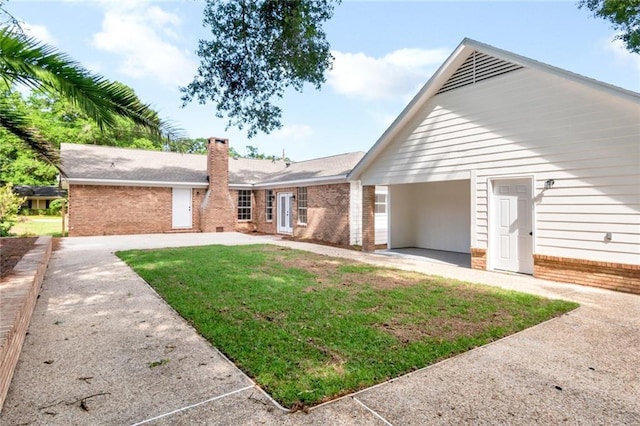 ranch-style home featuring brick siding, a front yard, a chimney, and a patio