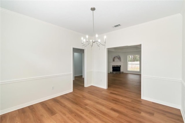 unfurnished dining area with baseboards, crown molding, a brick fireplace, light wood-type flooring, and a chandelier