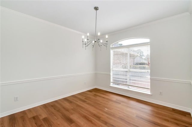 empty room featuring a chandelier, baseboards, wood finished floors, and ornamental molding