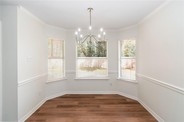 unfurnished dining area featuring baseboards, a notable chandelier, wood finished floors, and ornamental molding