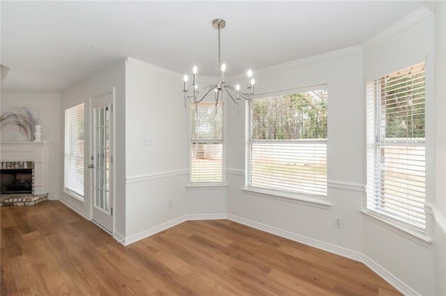 unfurnished dining area featuring a brick fireplace, a notable chandelier, wood finished floors, and baseboards