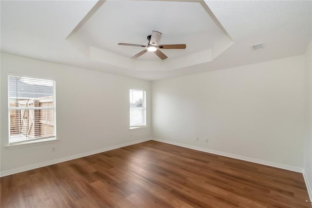 unfurnished room featuring visible vents, baseboards, a tray ceiling, wood finished floors, and a ceiling fan