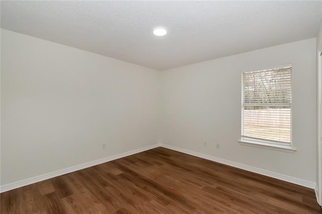 empty room with baseboards, dark wood-type flooring, and a textured ceiling