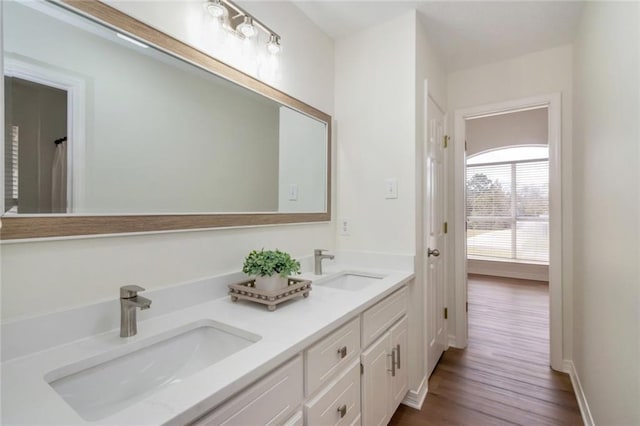 full bath with double vanity, wood finished floors, baseboards, and a sink