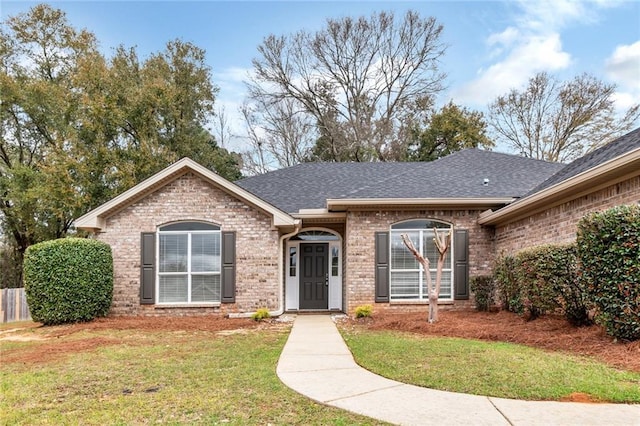 ranch-style home with brick siding, roof with shingles, and a front lawn