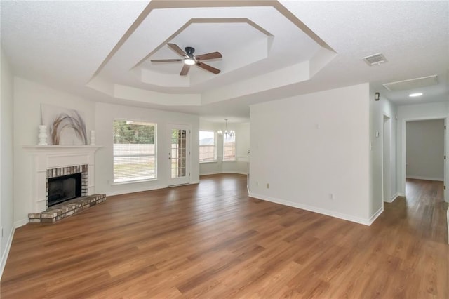 unfurnished living room featuring visible vents, a tray ceiling, light wood-style flooring, a fireplace, and a ceiling fan