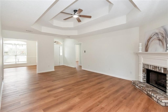 unfurnished living room with ceiling fan with notable chandelier, light wood-type flooring, a raised ceiling, and baseboards