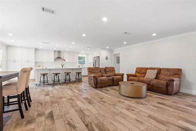 living room featuring light hardwood / wood-style floors, ornamental molding, and sink