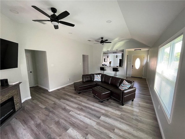 living room featuring a stone fireplace, wood-type flooring, vaulted ceiling, and ceiling fan