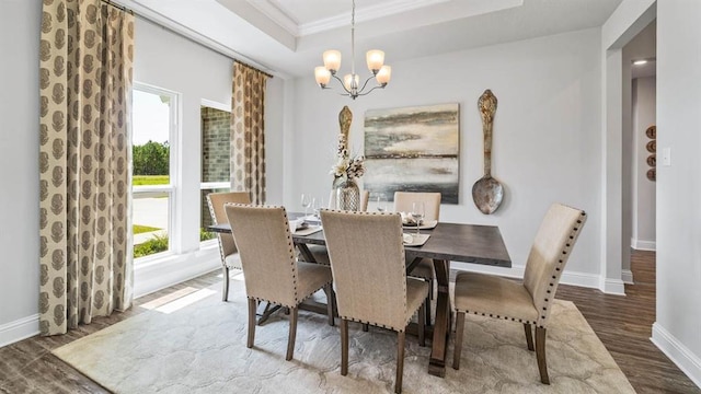 dining room featuring a raised ceiling, ornamental molding, dark wood-type flooring, and a chandelier