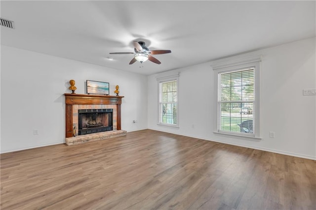 unfurnished living room with a fireplace, a ceiling fan, visible vents, baseboards, and wood finished floors