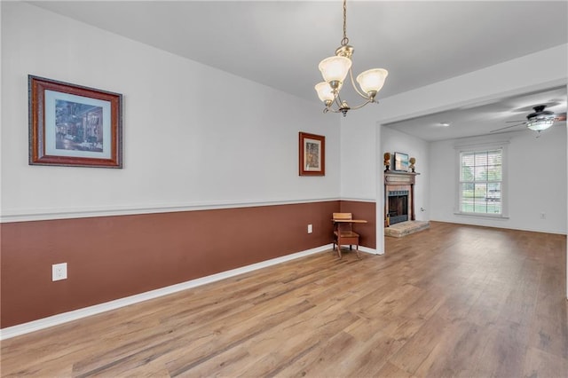 unfurnished living room featuring a fireplace with raised hearth, ceiling fan with notable chandelier, wood finished floors, and baseboards