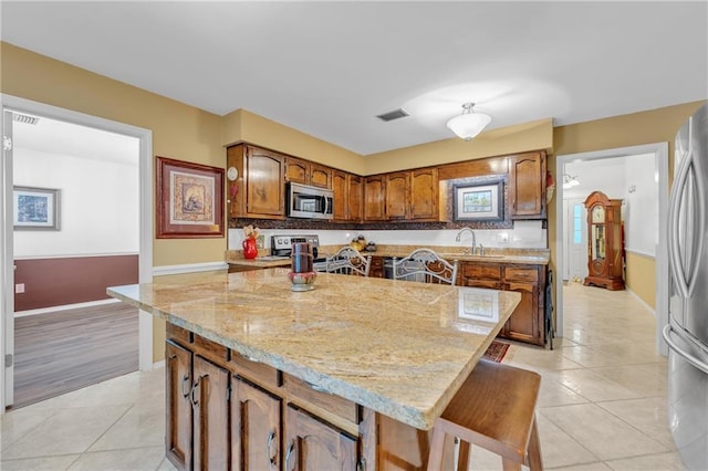 kitchen featuring a sink, light tile patterned floors, visible vents, a kitchen island, and appliances with stainless steel finishes