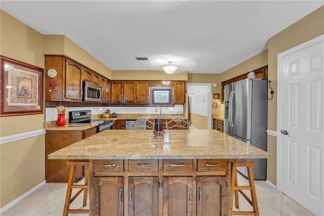 kitchen with a breakfast bar, appliances with stainless steel finishes, brown cabinets, a sink, and visible vents