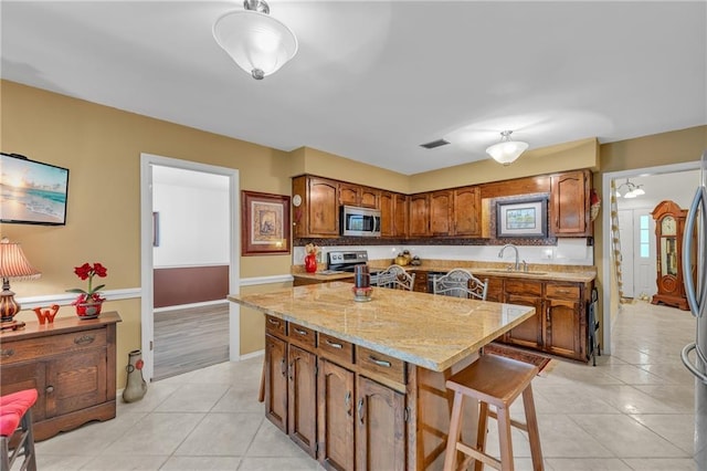 kitchen with light tile patterned floors, appliances with stainless steel finishes, a center island, a sink, and visible vents