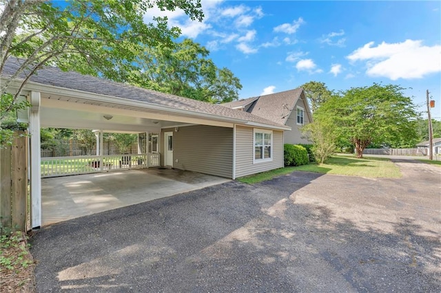 view of property exterior featuring fence, a carport, driveway, and a shingled roof