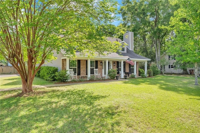view of front facade featuring a porch, a front lawn, a chimney, brick siding, and fence