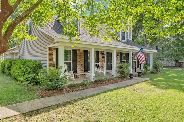 view of front of house with covered porch, brick siding, a shingled roof, and a front yard