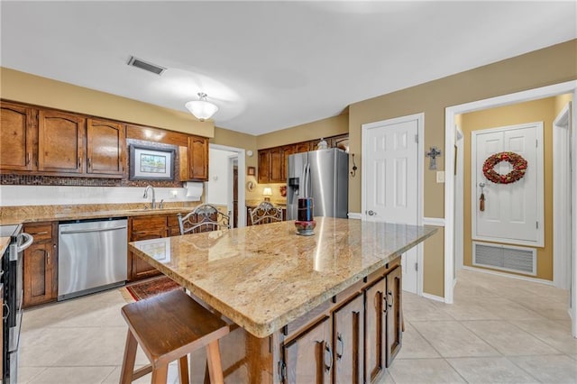 kitchen featuring light tile patterned floors, appliances with stainless steel finishes, visible vents, a center island, and brown cabinetry