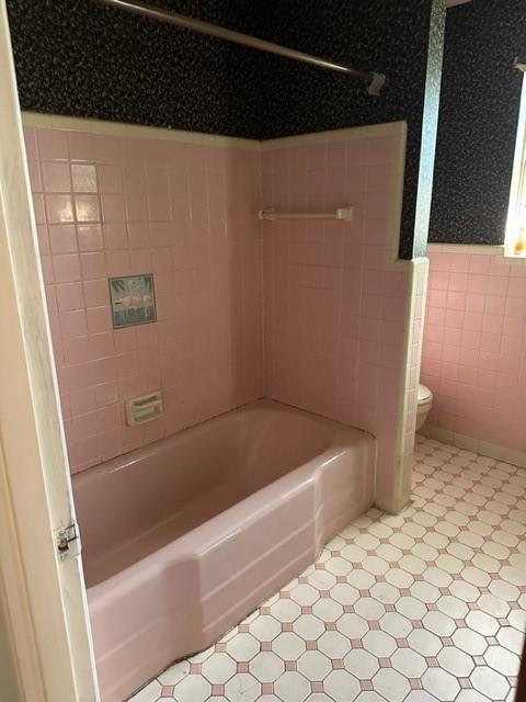 bathroom featuring shower / washtub combination, tile walls, and toilet