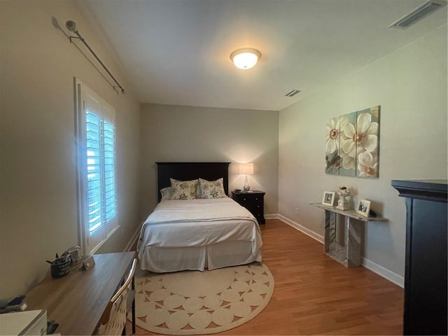 bedroom with baseboards, visible vents, and wood finished floors