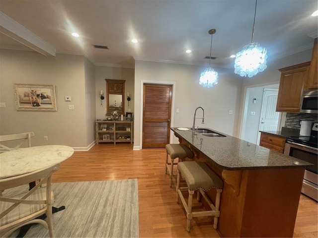 kitchen featuring appliances with stainless steel finishes, light wood-type flooring, a sink, and a kitchen breakfast bar