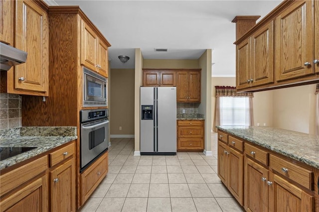 kitchen with light stone countertops, appliances with stainless steel finishes, light tile patterned floors, and backsplash