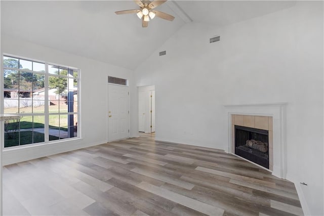 unfurnished living room with beam ceiling, ceiling fan, high vaulted ceiling, light hardwood / wood-style floors, and a tiled fireplace