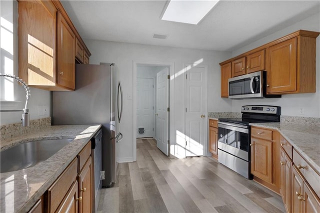 kitchen with light hardwood / wood-style floors, light stone counters, sink, and appliances with stainless steel finishes