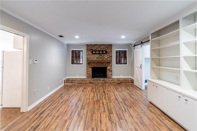 601 Willow Brook Run E, Mobile, AL 36608 - unfurnished living room with a barn door, crown molding, light wood finished floors, a brick fireplace, and recessed lighting