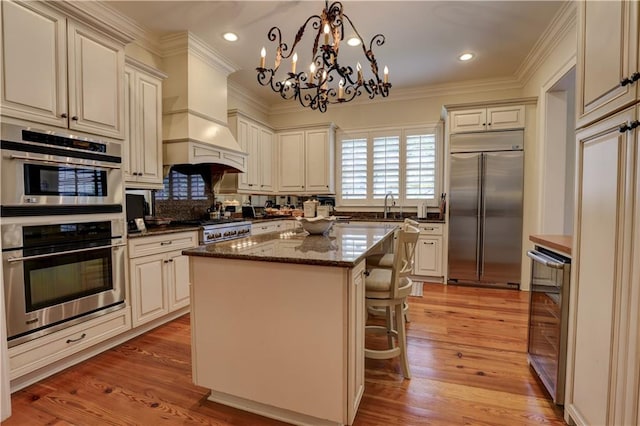 kitchen with decorative light fixtures, a chandelier, appliances with stainless steel finishes, a center island, and light wood-type flooring