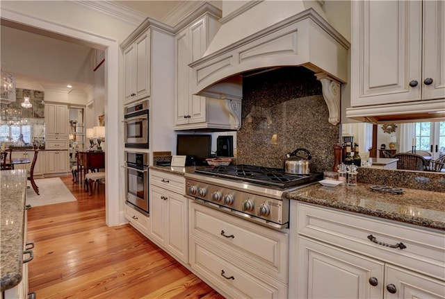 kitchen featuring stainless steel gas stovetop, custom exhaust hood, dark stone counters, and light hardwood / wood-style floors