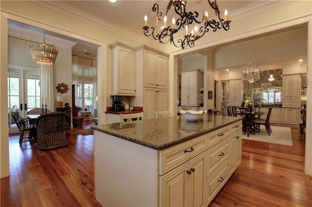 kitchen with a kitchen island, hardwood / wood-style floors, dark stone countertops, pendant lighting, and ornamental molding