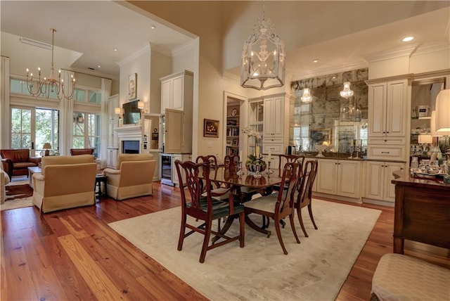 dining room with ornamental molding, a high ceiling, wine cooler, and light hardwood / wood-style flooring