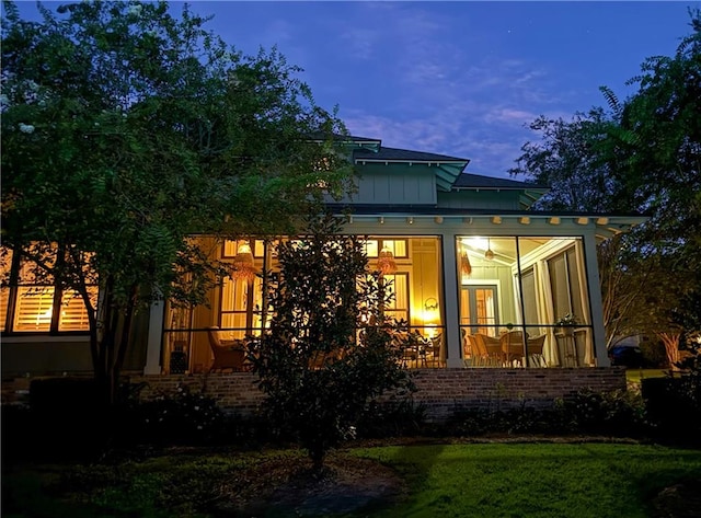 back house at dusk featuring a sunroom and a lawn