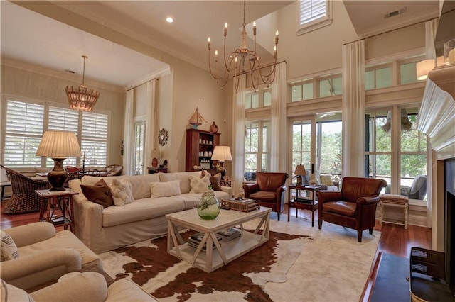 living room with a towering ceiling, a chandelier, hardwood / wood-style floors, and crown molding