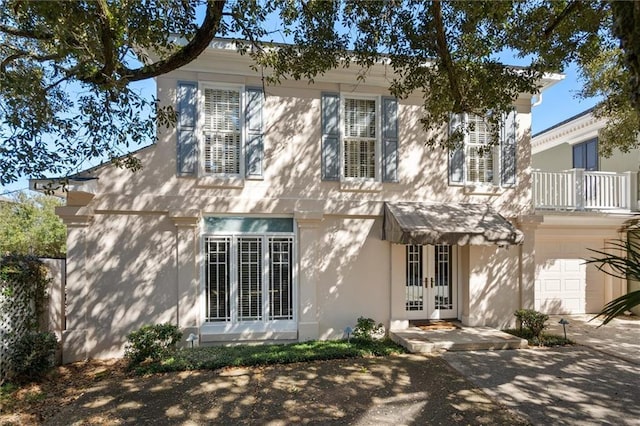 view of front of house with a balcony, stucco siding, french doors, and a garage