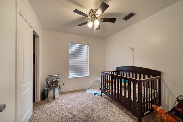 carpeted bedroom featuring a ceiling fan, a closet, baseboards, a nursery area, and visible vents