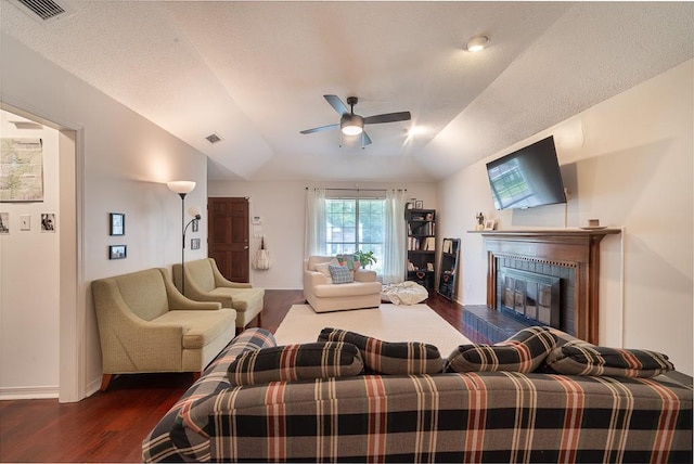 living room featuring dark wood-style flooring, a glass covered fireplace, a ceiling fan, and visible vents