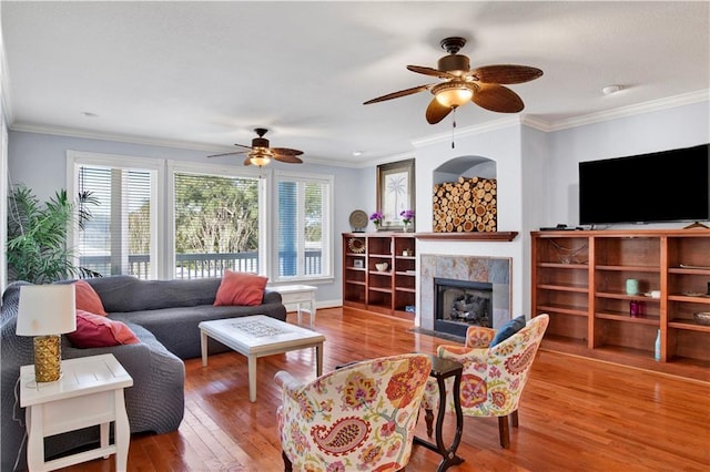 living room featuring a tiled fireplace, wood-type flooring, and ornamental molding